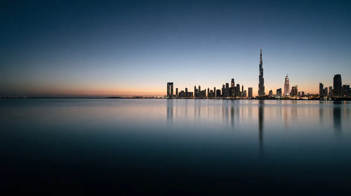 The Dubai skyline and the Burj Khalifa across still water just after sunset